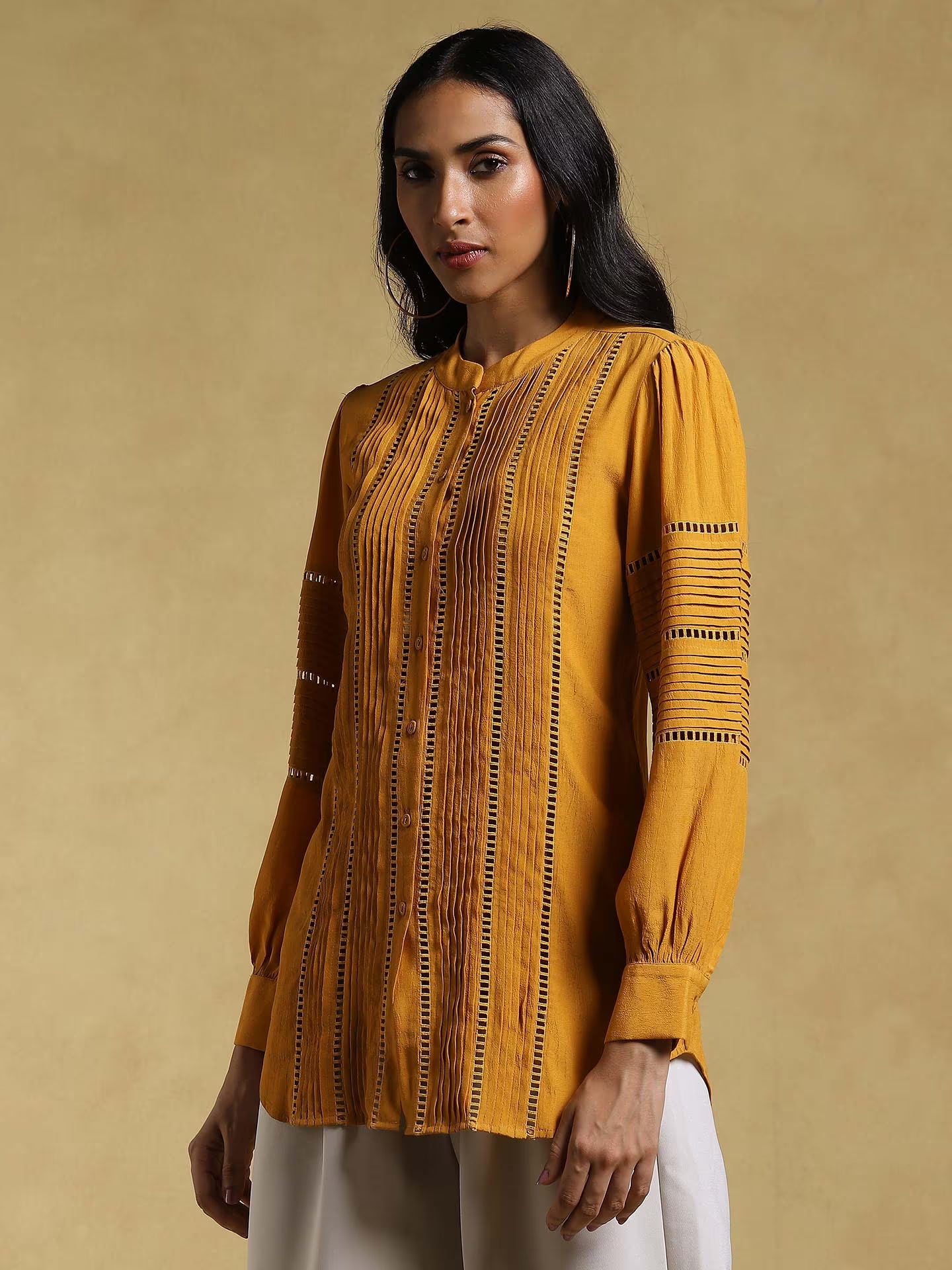 Woman wearing a mustard yellow patterned top against a beige background