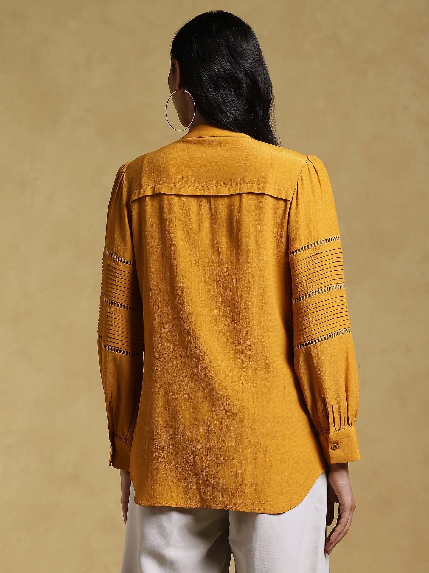 Woman wearing a mustard yellow blouse with intricate patterns on a beige background
